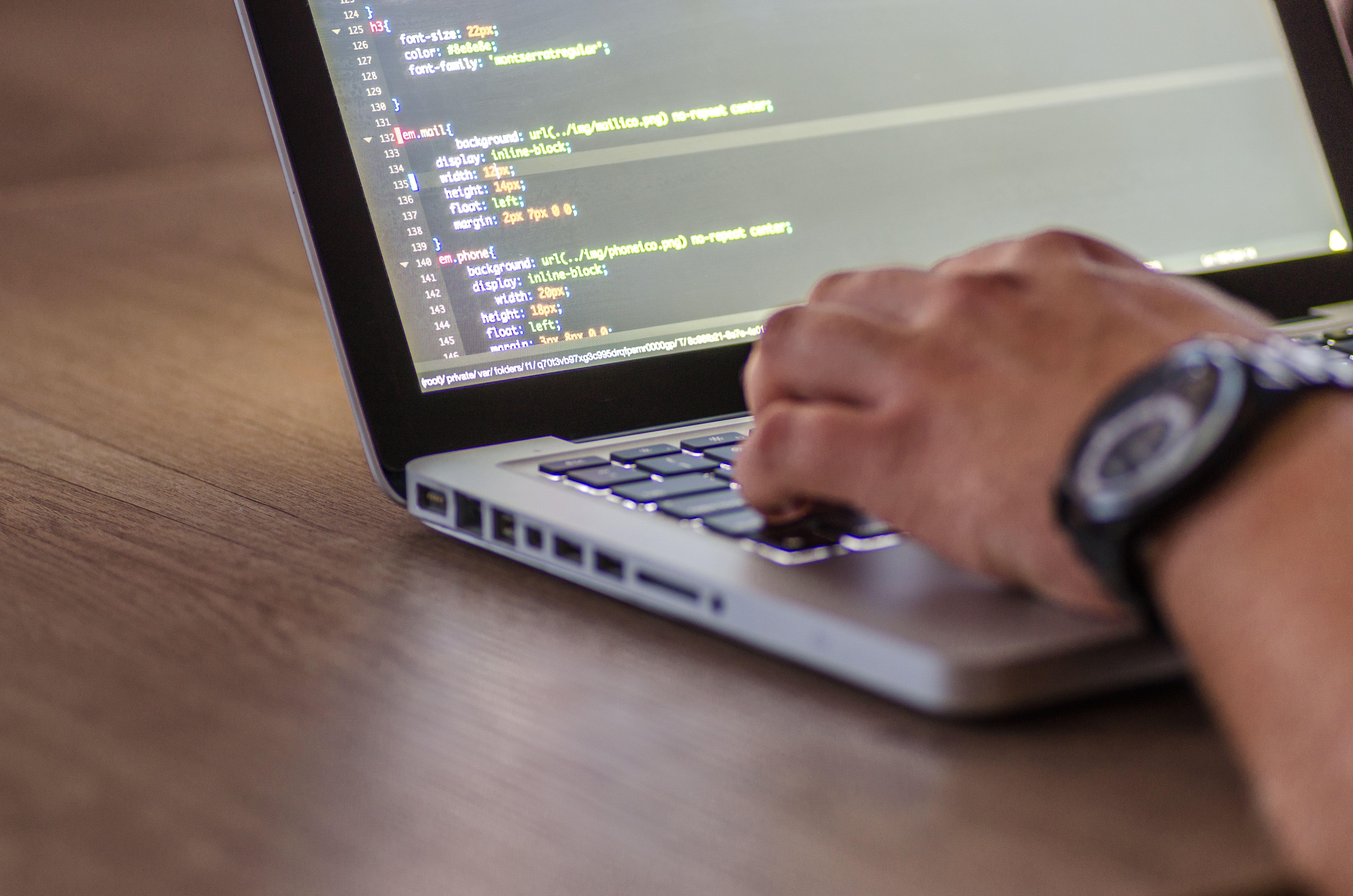 A person's hands writing code on a Mac laptop